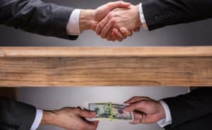 Two people shaking hands also exchanging money under a table